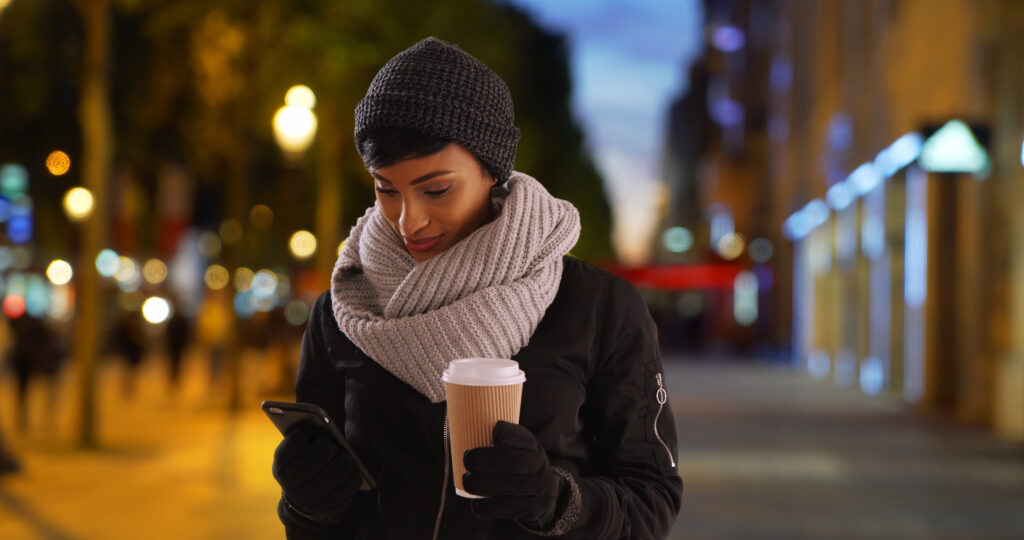 Women with warm coffee and phone in hand, dressed in winter clothing.